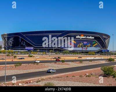 Las Vegas, NV, USA - 12. Mai 2024: Schwarzes Allegiant Stadium hinter der interstate 15 mit internationalem Fußballschild unter blauem Himmel. Leerer Parkplatz, Autos an Stockfoto