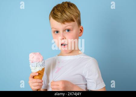 Der Junge ist überrascht, schmutzige Flecken von Eis auf Ihrer Kleidung auf einem blauen Hintergrund. Daily Life Fleck und Reinigungskonzept Stockfoto