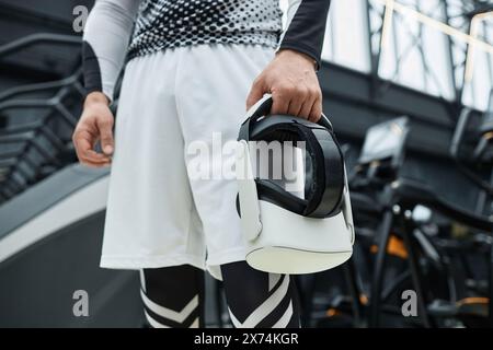 Nahaufnahme eines nicht erkennbaren Mannes, der das VR-Headset in der Hand hält, mit Trainingsgeräten im Hintergrund im Kopierraum Stockfoto