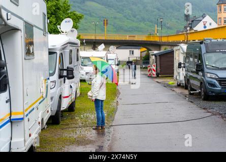 Zeltingen Rachtig, Deutschland. Mai 2024. Eine Frau steht mit einem bunten Regenschirm neben ihrem Wohnmobil auf einem erhöhten Gelände des Zeltinger Wohnmobilstandortes. Die Uferbereiche mussten evakuiert werden. Das Hochwassermeldezentrum schätzt, dass der Wasserstand der Mosel bis Sonntag auf 7,30 Meter steigen wird. Die B49 am Flussufer würde dann ebenfalls überflutet und musste geschlossen werden. Das Wasser würde dann auch die Altstadt von Cochem erreichen. Einige Standorte für Wohnmobile und Wohnwagen in der Nähe der Moselufer mussten evakuiert werden. Darlegung: Andreas Arnold/dpa/Alamy Live News Stockfoto