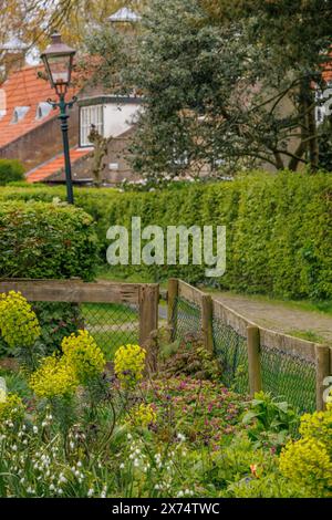 Ein gepflegter Holzzaun mit blühenden Geländerblumen entlang der ruhigen Dorfstraße, alte Häuser mit grünen Gärten in einem kleinen Dorf Stockfoto