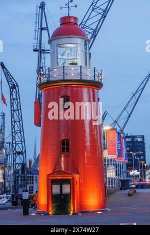 Ein markanter roter Leuchtturm, beleuchtet bei Nacht, umgeben von Hafenkranen und Gebäuden, kleiner Hafen in einer großen Stadt mit einem Leuchtturm und modern Stockfoto