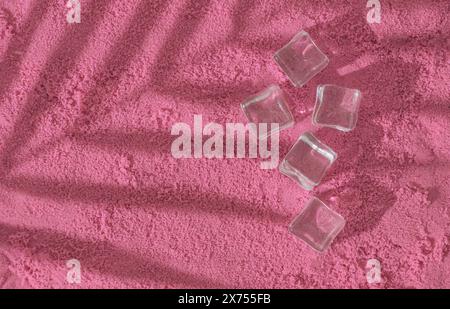 Tropische Palmenblattschatten und Eiswürfel auf rosafarbenem Sandhintergrund. Sommerliche ästhetische Idee. Minimales Konzeptfoto von Sommerferien. Stockfoto