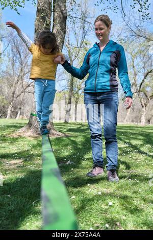 Mutter unterstützt den Sohn beim Slacklining im Park Stockfoto