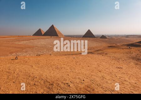 Großer Blick auf die drei Pyramiden von Gizeh – Khufu, Khafre und Menkaure – im frühen Licht über der Wüste mit einer trüben Skyline von Kairo in der Ferne. Stockfoto