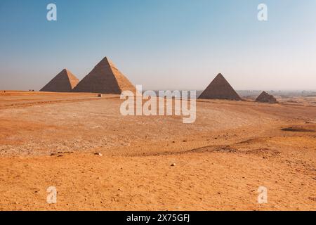 Großer Blick auf die drei Pyramiden von Gizeh – Khufu, Khafre und Menkaure – im frühen Licht über der Wüste mit einer trüben Skyline von Kairo in der Ferne. Stockfoto