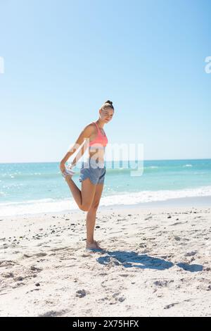 Am Strand, kaukasische junge Frau, die sich ausdehnt und den Fuß hält Stockfoto