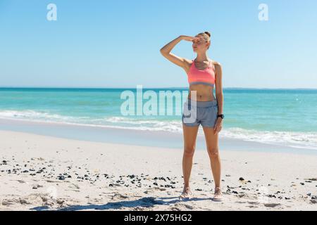 Am Strand, eine junge kaukasische Frau, die die Augen vor der Sonne schützt Stockfoto