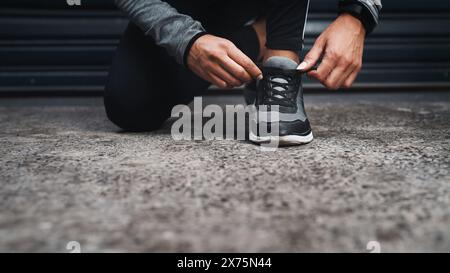 Hände, Fitness- und Krawattenschuhe auf dem Boden für Training, Workout oder Läufertraining im Freien in der Stadt. Turnschuhe, Beine und Frau, die auf dem Bürgersteig Spitzen schnürt Stockfoto