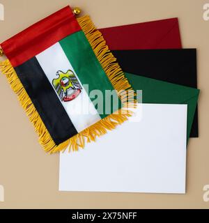Kleine Flagge der VAE auf beigefarbenem Hintergrund mit bunten Umschlägen. Kopierbereich. Vorlage für Werbeanzeigen vortäuschen. Reisegutschein mit dem nationalen Symbol der Vereinigten Arabischen Emirate. Besuchen Sie Dubai Concept Stockfoto
