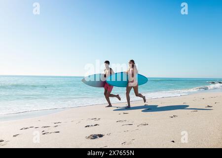 Am Strand gibt es diverse Paare mit Surfbrettern, die auf Sand laufen Stockfoto