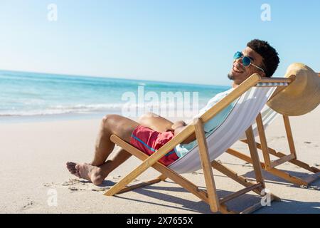 Am Strand, junger Mann, der sich auf Liegen entspannt, Sonne genießt, Kopierraum Stockfoto