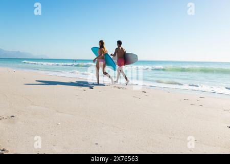 Am Strand gibt es diverse Paare mit Surfbrettern, die auf Sand laufen Stockfoto