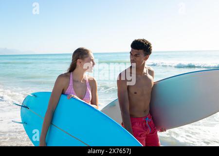 Am Strand, verschiedene Paare halten Surfbretter und schauen sich gegenseitig an Stockfoto