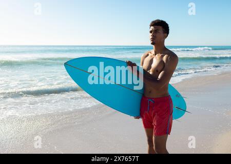 Am Strand, junger Mann mit blauem Surfbrett und Blick auf das Meer Stockfoto