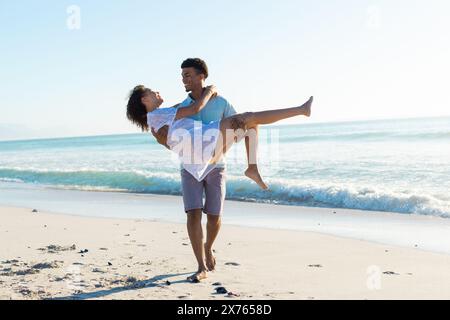 Am Strand lacht ein Paar, ein Mann trägt eine Frau Stockfoto