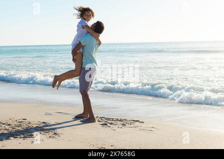 Am Strand genießt ein birassisches Paar die Zeit, männliche, weibliche, hebende Frauen Stockfoto