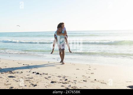 Am Strand genießen verschiedene Paare einen Huckepack-Ritt und lachen zusammen Stockfoto