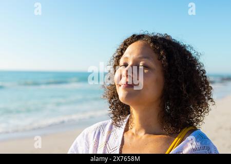 Am Strand steht eine junge Frau mit birassischer Herkunft, genießt Sonne und Kopierraum Stockfoto