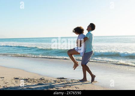 Am Strand genießt ein birassisches Paar die Zeit, männliche, weibliche, hebende Frauen Stockfoto