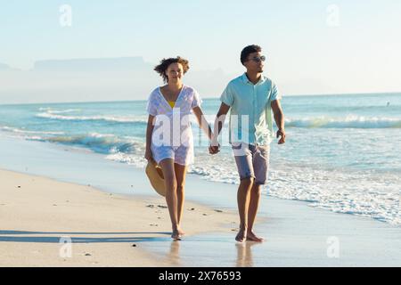 Am Strand hält ein birassisches Paar Hände und läuft Stockfoto