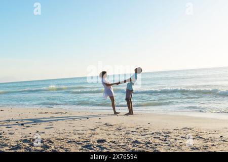 Am Strand hält ein birassisches Paar Hände und sieht sich an Stockfoto