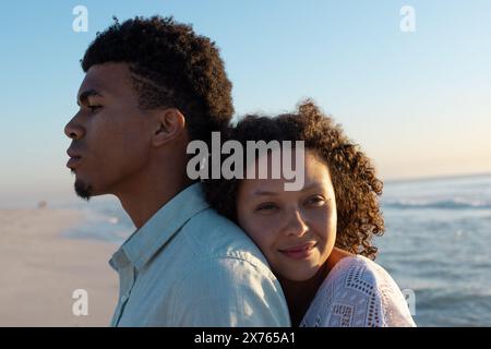 Am Strand steht ein birassisches Paar, eine Frau, die Kopf auf der Schulter des Mannes liegt Stockfoto