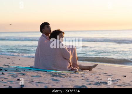 Am Strand, zweirassige Paare, in Decke gehüllt, auf das Meer blickend Stockfoto