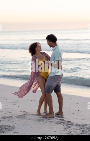 Am Strand hält ein birassisches Paar Hände und lacht zusammen Stockfoto