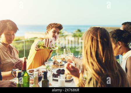 Freunde, Wein und Party mit Essen, Feiern und Alkohol zusammen mit Glas und jungen Leuten auf dem Dach. Veranstaltung, Getränke und Essen im Urlaub in Stockfoto