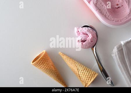 Löffel mit Kugel Erdbeereis isoliert auf weißem Tisch mit Eiskegel und Wanne. Draufsicht. Stockfoto