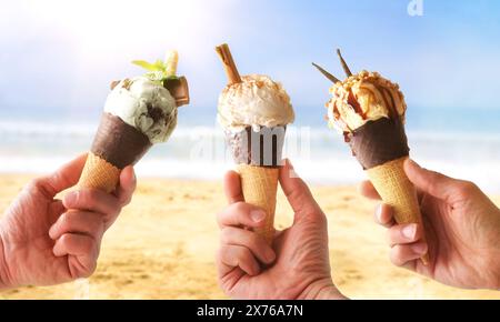 Drei Hände halten Eiskegel mit verschiedenen Urlaubsgeschmack am Strand Stockfoto