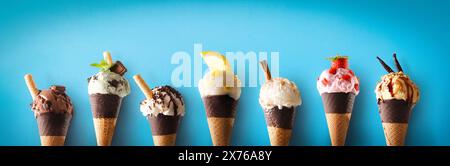 Auswahl an Eiskegeln mit verschiedenen Geschmacksrichtungen in einer Reihe mit Schokoladentegel auf blauem Hintergrund. Stockfoto