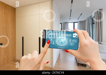 Nahaufnahme Smartphone in weiblicher Hand mit Smart-Home-System-App-Schnittstelle auf Handybildschirm, junge Frau, die alle Systeme des Hauses per Telefon steuert Stockfoto