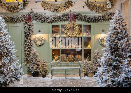 Neujahrsfotozone mit Schnee in der Nähe einer Café-Bäckerei. Weihnachtsdekoration: Spielzeug, Weihnachtsbäume, Bank, Girlande, glühende Glühbirnen. Festliche Stimmung. Bild Stockfoto