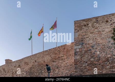 Drei Flaggen fliegen bei Sonnenuntergang an den Mauern der alten Burg Gibralfaro in Malaga, Spanien Stockfoto