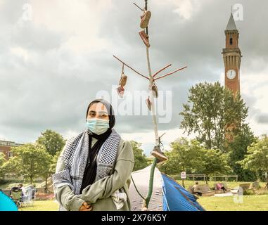 Ein Student mit einer Gesichtsmaske im Pro-palästinensischen Protestlager an der Universität Birmingham. Der alte Joe, der Uhrturm im Hintergrund. Stockfoto