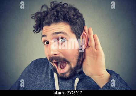 Nahaufnahme Porträt eines jungen, neugierigen, schockierten Mannes Hand-zu-Ohr-Geste, vorsichtig, insgeheim einem Klatsch zuhört, einem Gespräch Stockfoto