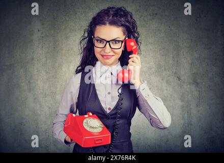 Lächelnde, glückliche junge Frau, die auf einem alten Telefon spricht Stockfoto