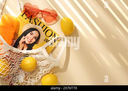 Schnur-Tasche mit frischen Zitronen, Modemagazin und Strandaccessoires auf beigefarbenem Hintergrund, flacher Lay. Leerzeichen für Text Stockfoto