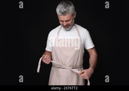 Mann mit Küchenschürze auf schwarzem Hintergrund. Modell für Design Stockfoto