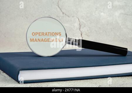 Betriebsmanagement-Geschäftskonzept. BETRIEBSMANAGEMENT geschrieben. Durch eine Lupe, die auf einem Geschäftsbuch auf grauem Hintergrund steht Stockfoto