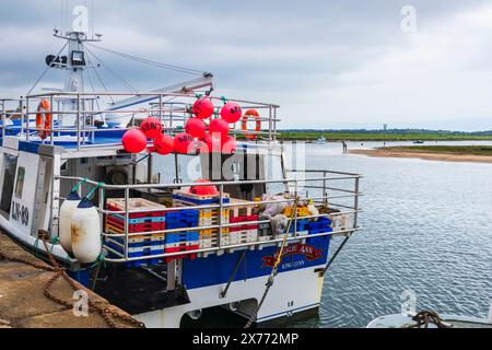 Großes Fischerboot, das an einem bewölkten Tag im Mai in Wells-next-the-Sea mit rosa Bojen und Fischboxen vor Anker liegt Stockfoto