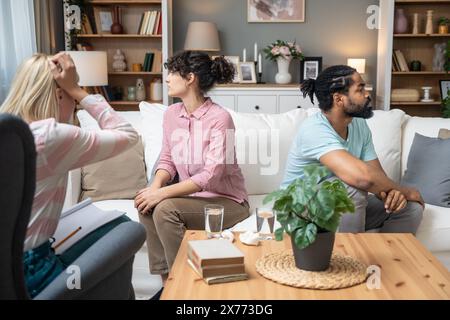 Ernsthafte junge Mann und Frau im Gespräch mit Psychologin beschweren sich über schlechte Beziehungsschwierigkeiten zwischen Ehemann und Ehefrau. Familienpaarberatung Stockfoto