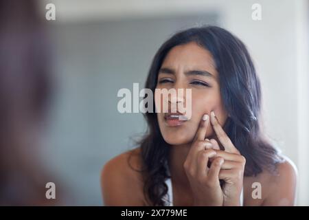 Frustriert, Frau und Gesicht mit der Hand für Pickel, der in Spiegelreflexe für Hautpflege, Pflege und Morgenroutine auftaucht. Inder, weibliche Person und Stockfoto