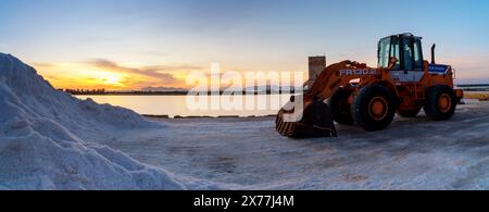 Paceco, Italien - 3. Januar 2024: Frontlader und Seesalzhaufen in der Salzebene von Trapani und Paceco bei Sonnenuntergang Stockfoto