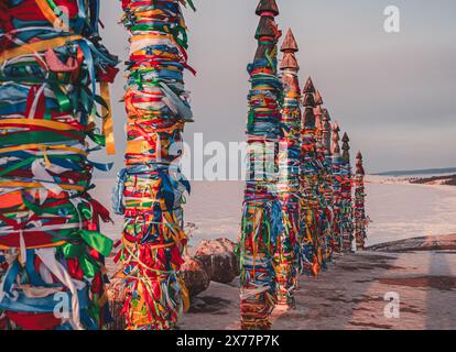 Traditionelle buryat Schamanen-Säulen mit bunten Bändern im Winter bei Sonnenuntergang, Kap Burkhan, Olkhon Insel. Winter Baikal. Stockfoto