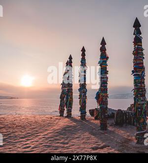Traditionelle buryat Schamanen-Säulen mit bunten Bändern im Winter bei Sonnenuntergang, Kap Burkhan, Olkhon Insel. Winter Baikal. Stockfoto