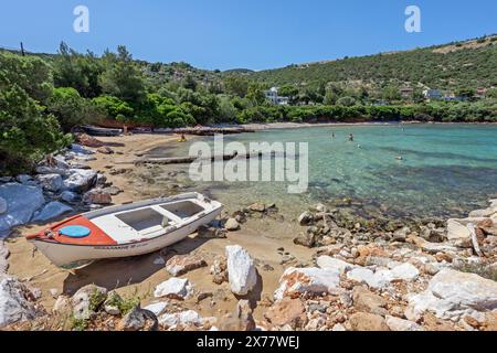 Agia Marina Beach mit einem traditionellen Holzboot und einige Leute genießen das kristallklare türkisfarbene Wasser dieses abseits der Touristenpfade Sandstrand. Stockfoto