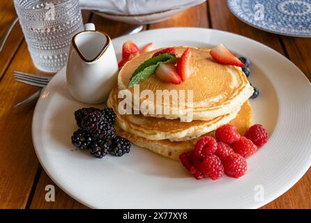 Stapel Pfannkuchen mit Erdbeeren, Brombeeren und Himbeeren auf einem weißen Teller mit einem kleinen Sirup auf einem Tisch in einem Restaurant Stockfoto